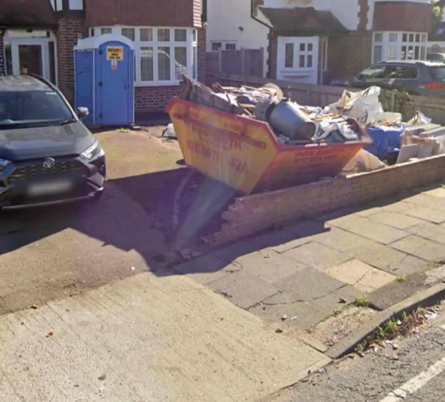 The original driveway before work started: worn concrete and tarmac, a skip on the frontage and the old low boundary wall partly removed.