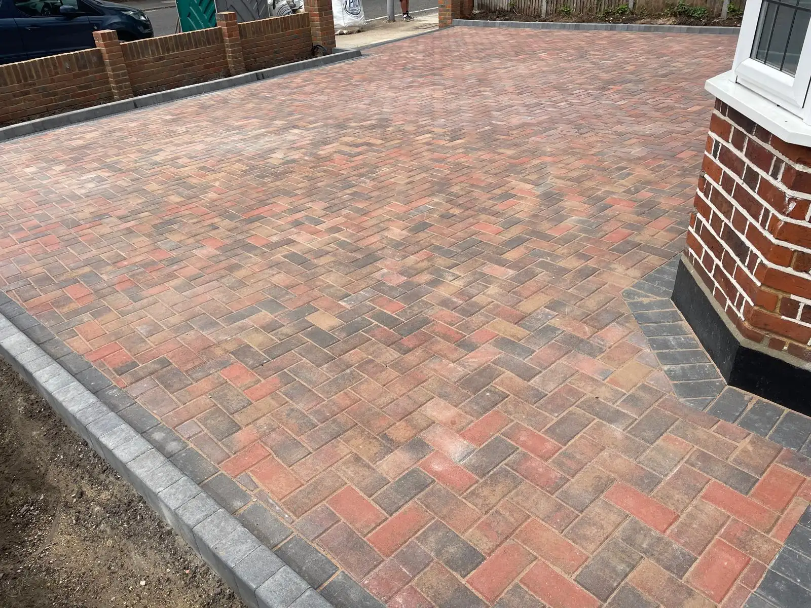 A finished brindle block paved driveway taken neatly around the bay window with a charcoal border, and a low brick boundary wall separating it from the pavement.