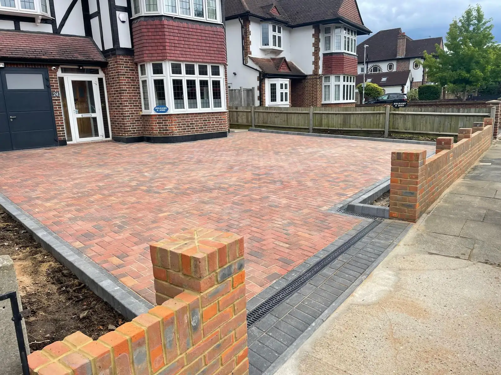 A completed block paved driveway in front of a 1930s semi-detached house, with a charcoal border, brick piers and a low front boundary wall.