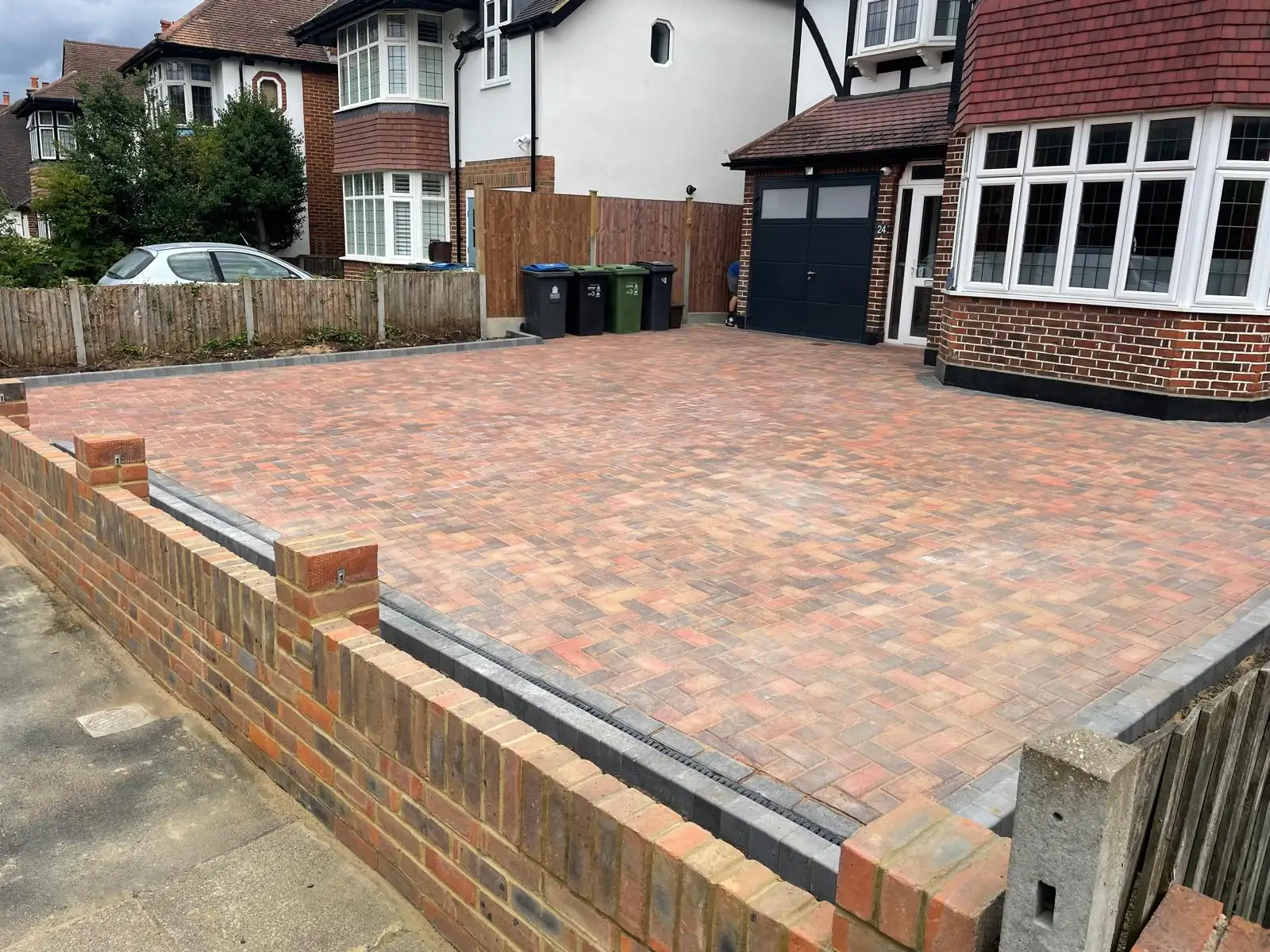 The finished driveway seen from the side, showing the full parking area, the charcoal border running to the garage and the rebuilt brick boundary wall with piers.