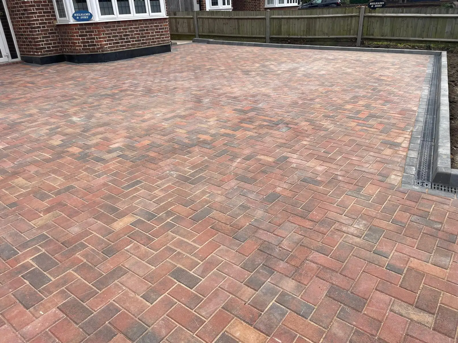 Close detail of a completed brindle block paved driveway laid in herringbone, with tight joints and a linear channel drain running along the charcoal edge course.